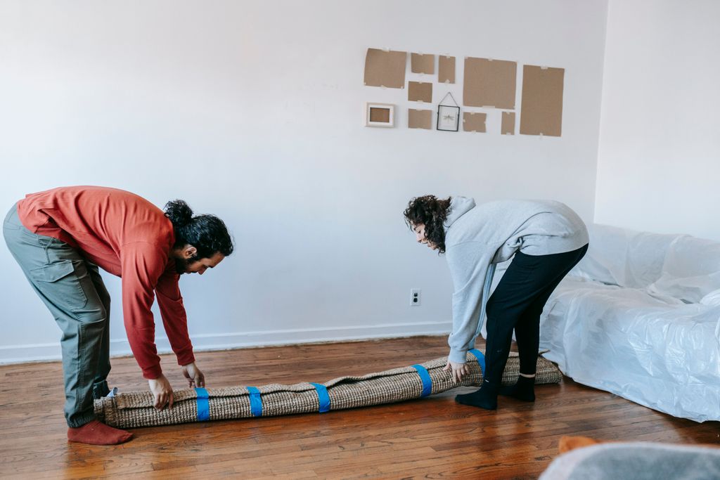 Two adults carefully roll up a rug while packing up in a bright, minimal living room.