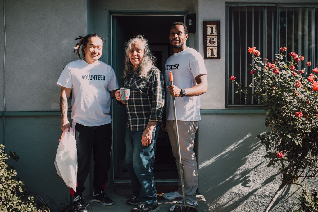 Two volunteers assist a community member outside their home, fostering social good.