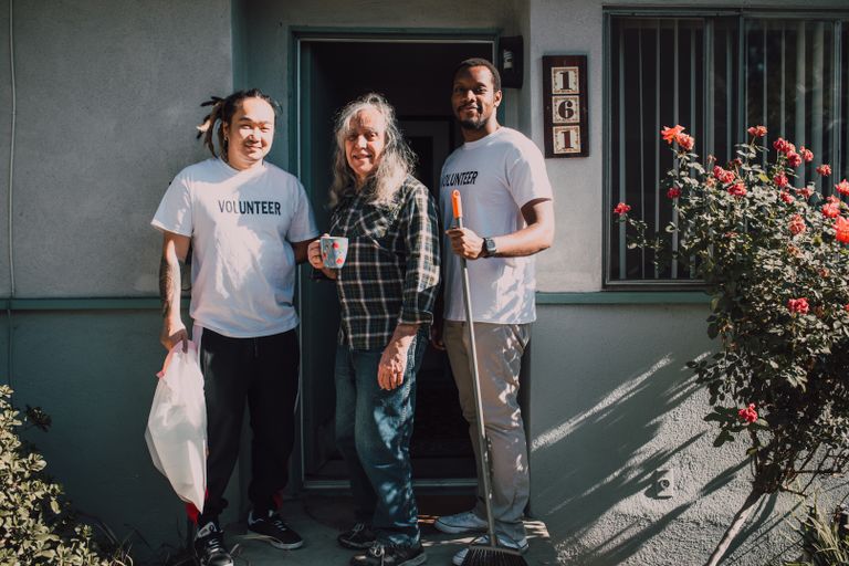 Two volunteers assist a community member outside their home, fostering social good.