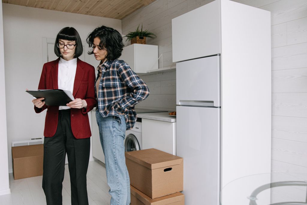 Two women reviewing documents in a kitchen amid moving boxes.