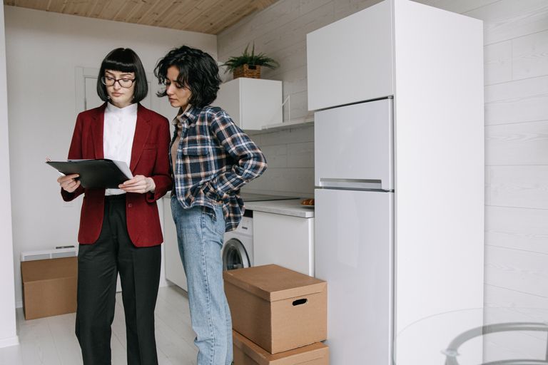 Two women reviewing documents in a kitchen amid moving boxes.